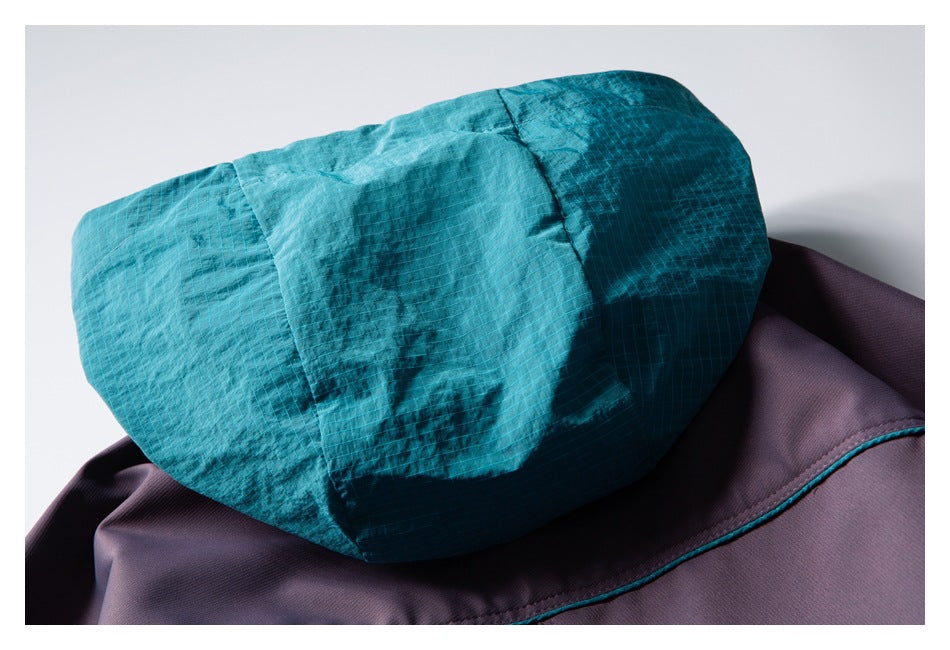 Close-up of a teal hood with stitched panels resting against a purple garment.