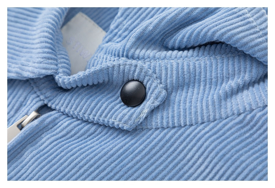 Close-up of a black snap fastener on the light blue corduroy jacket beside its zipper.