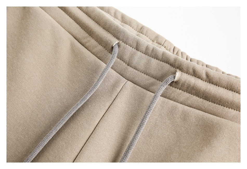 Close-up of beige pants showing an elastic waistband, center seam, and gray drawstrings.