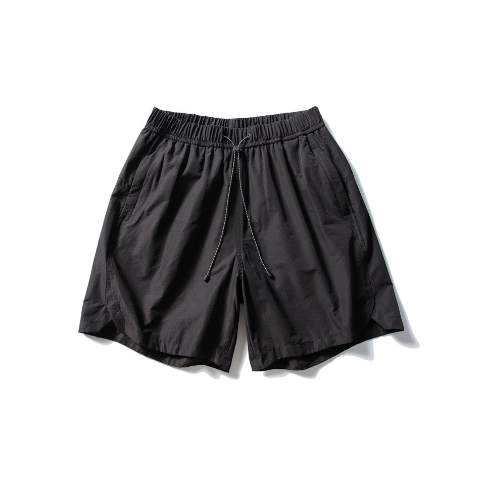 Black drawstring shorts with elastic waistband, side pockets and curved side-slit hems, flat lay