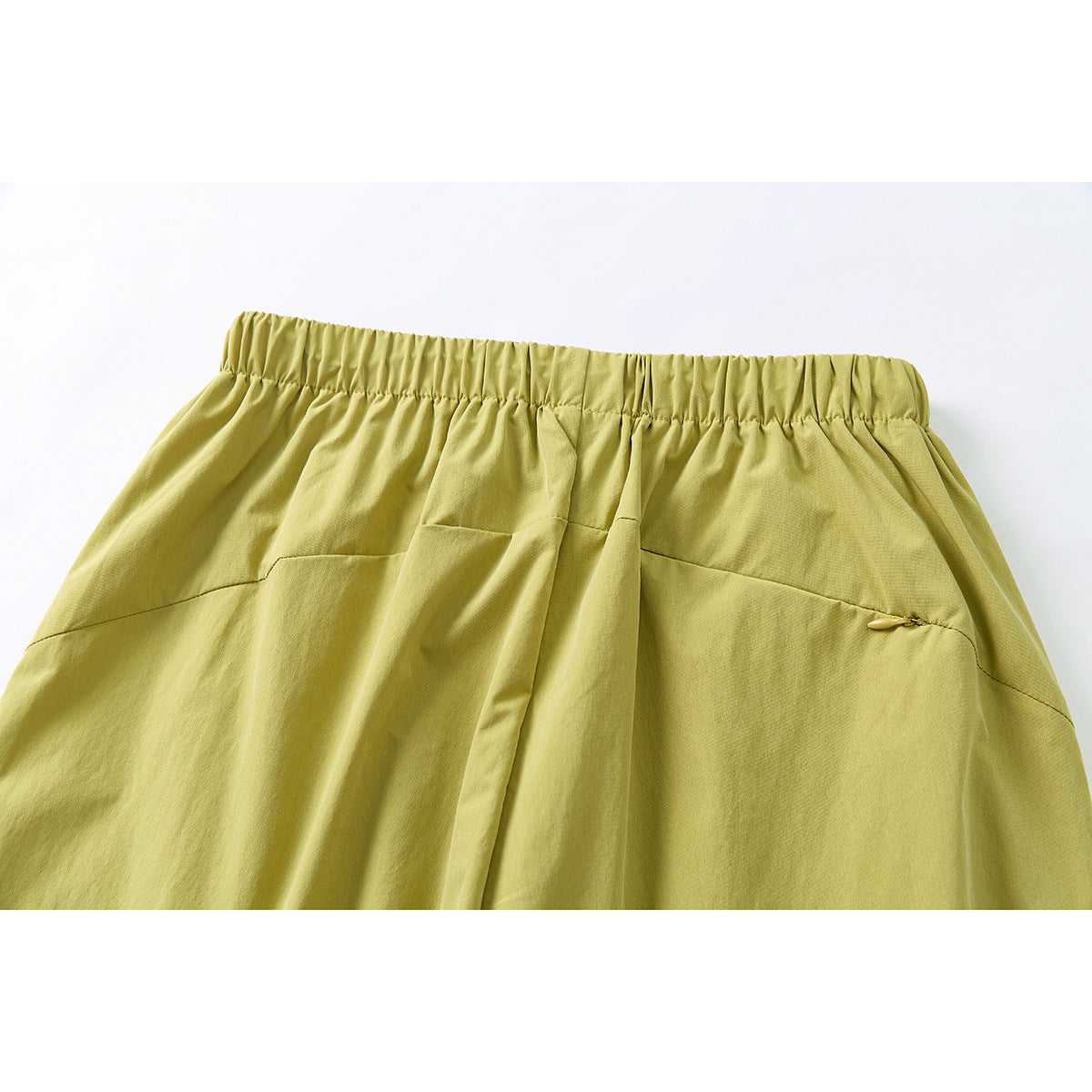 Close-up of the back waistband of mustard yellow-green trousers with elastic gathering and a small pocket.