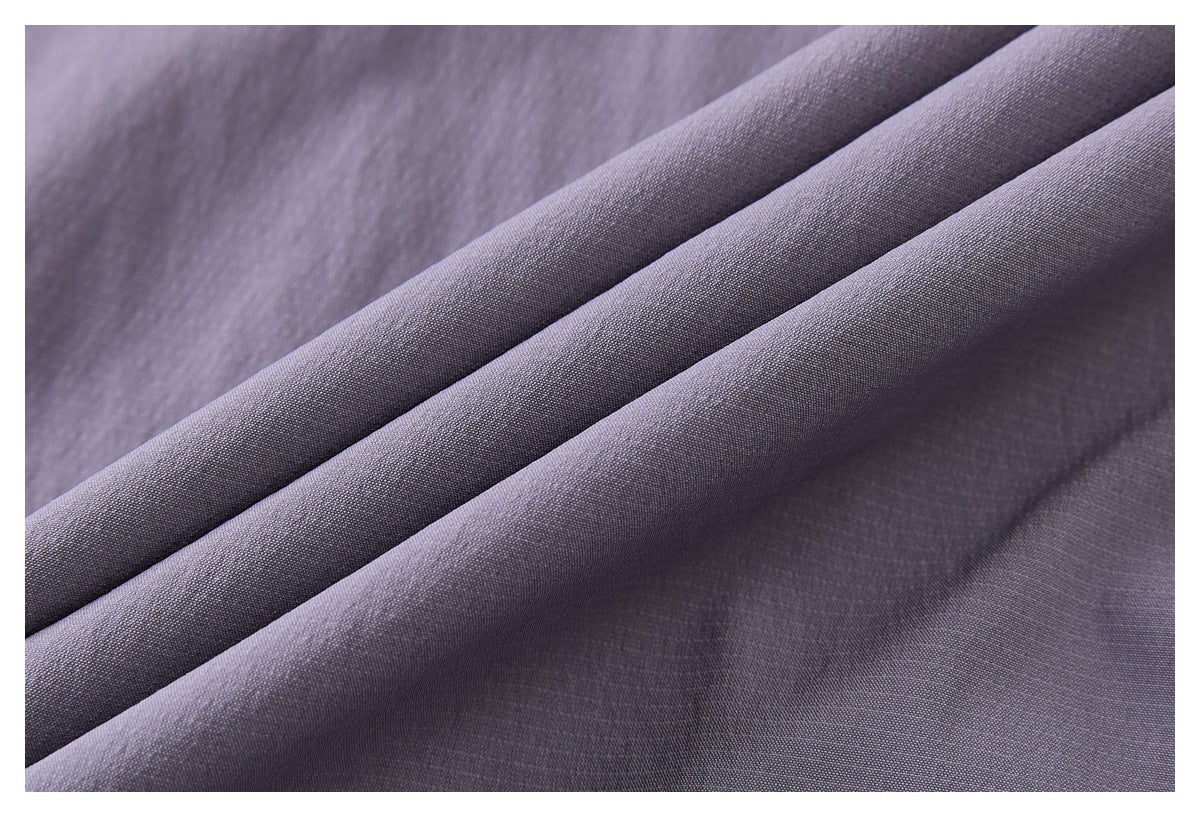 Close-up of muted lavender-gray fabric folded into diagonal folds, showing its fine surface texture.