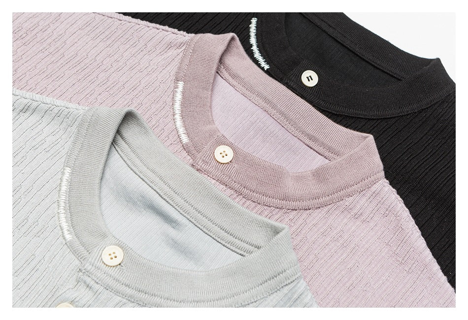 Close-up of three textured knit tops in pale gray, mauve, and black, showing round necklines and buttons.