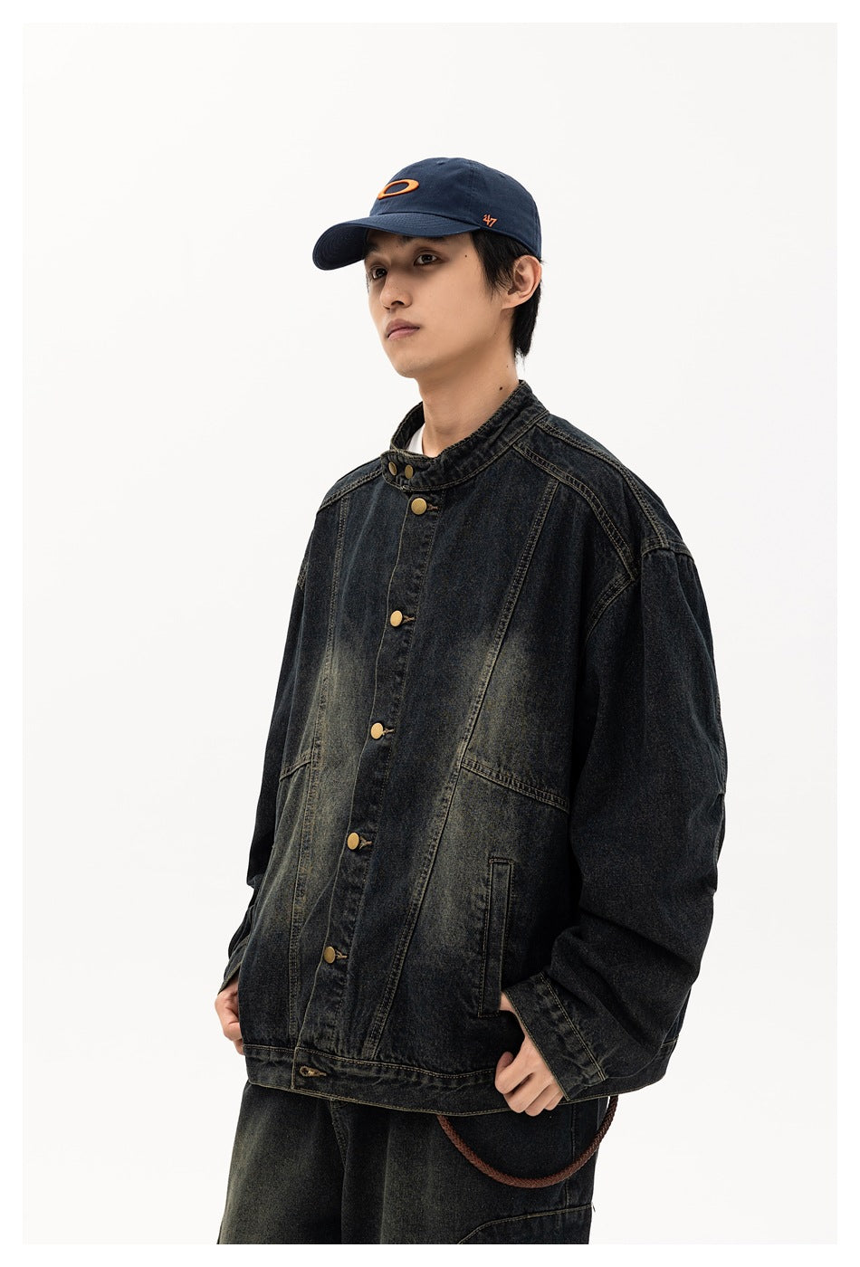 Model wearing an oversized black washed-denim jacket with a stand collar and brass buttons, shown from the front.