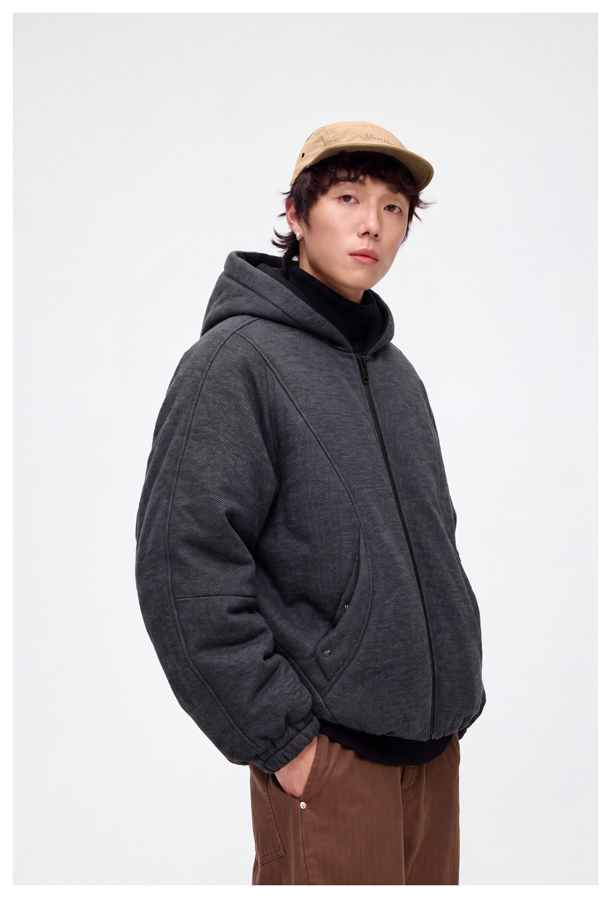 Three-quarter front view of a model wearing a charcoal hooded jacket with a black front zipper and curved pockets.