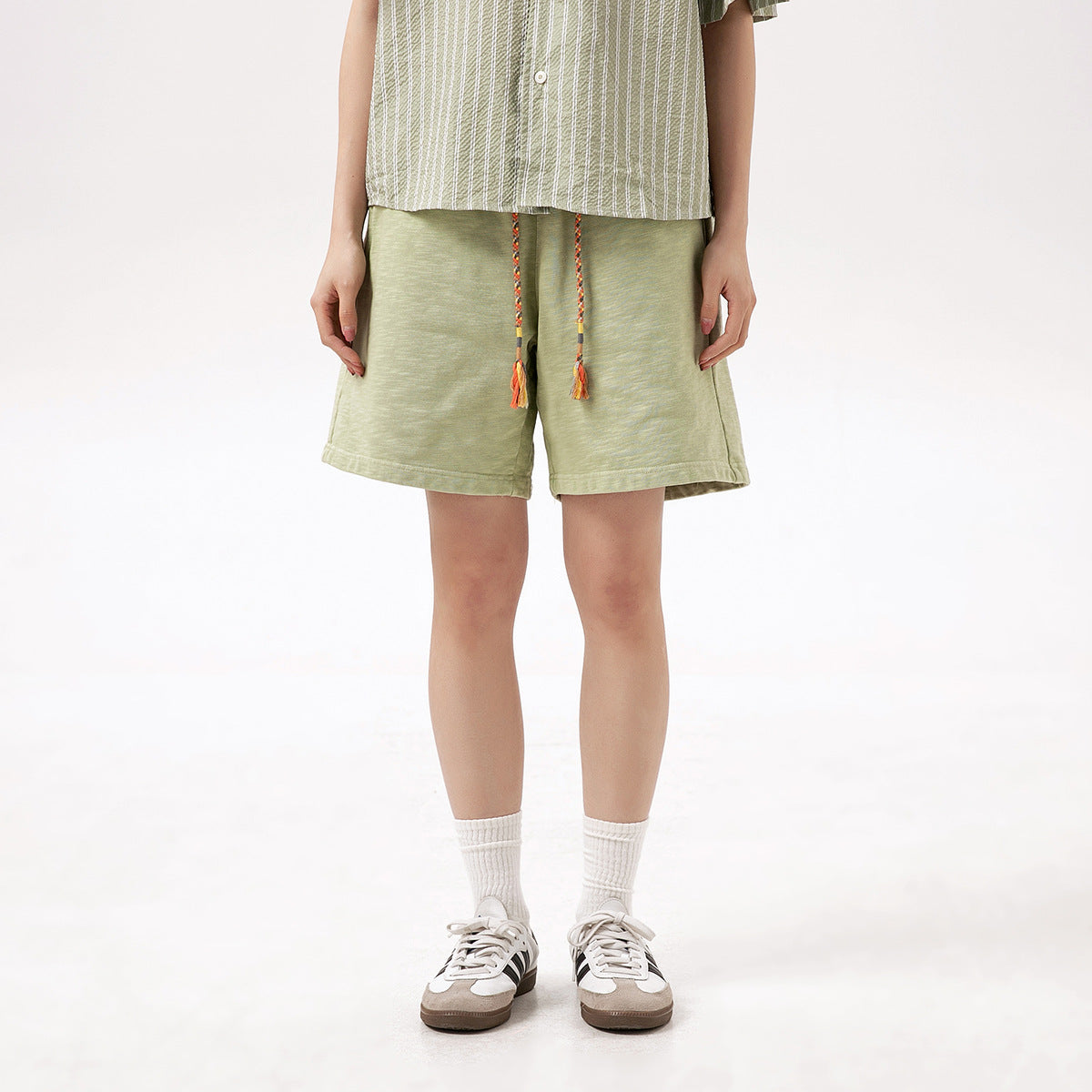 Front view of a model wearing pale sage green shorts with braided drawstrings and tassels.
