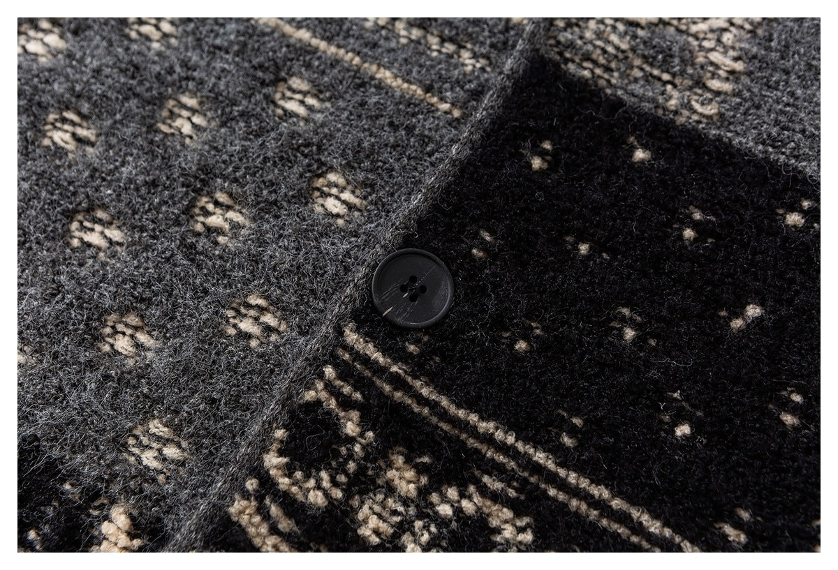 Close-up of a black button and textured black, gray, and cream patterned knit fabric.