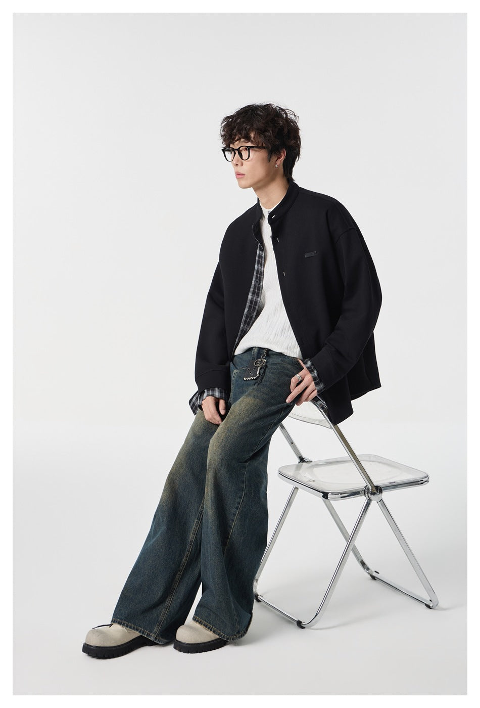 Seated model wearing a black plaid-trim stand-collar jacket with wide-leg jeans.