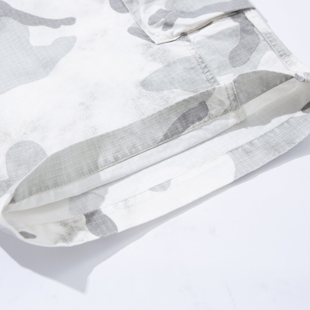 Close-up of the stitched hem on gray and white camouflage shorts.