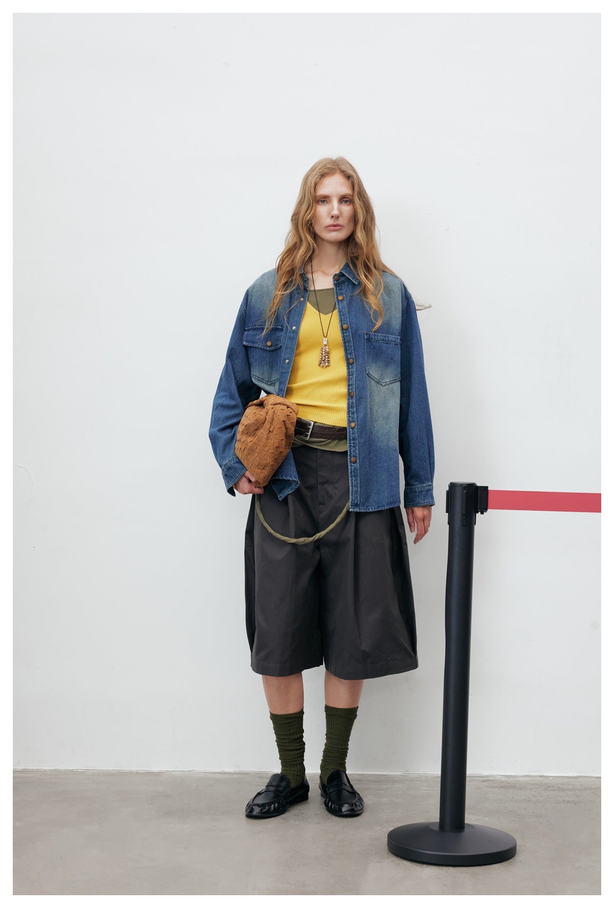 Model wearing the blue washed denim shirt-jacket open over a yellow top with dark wide-leg shorts