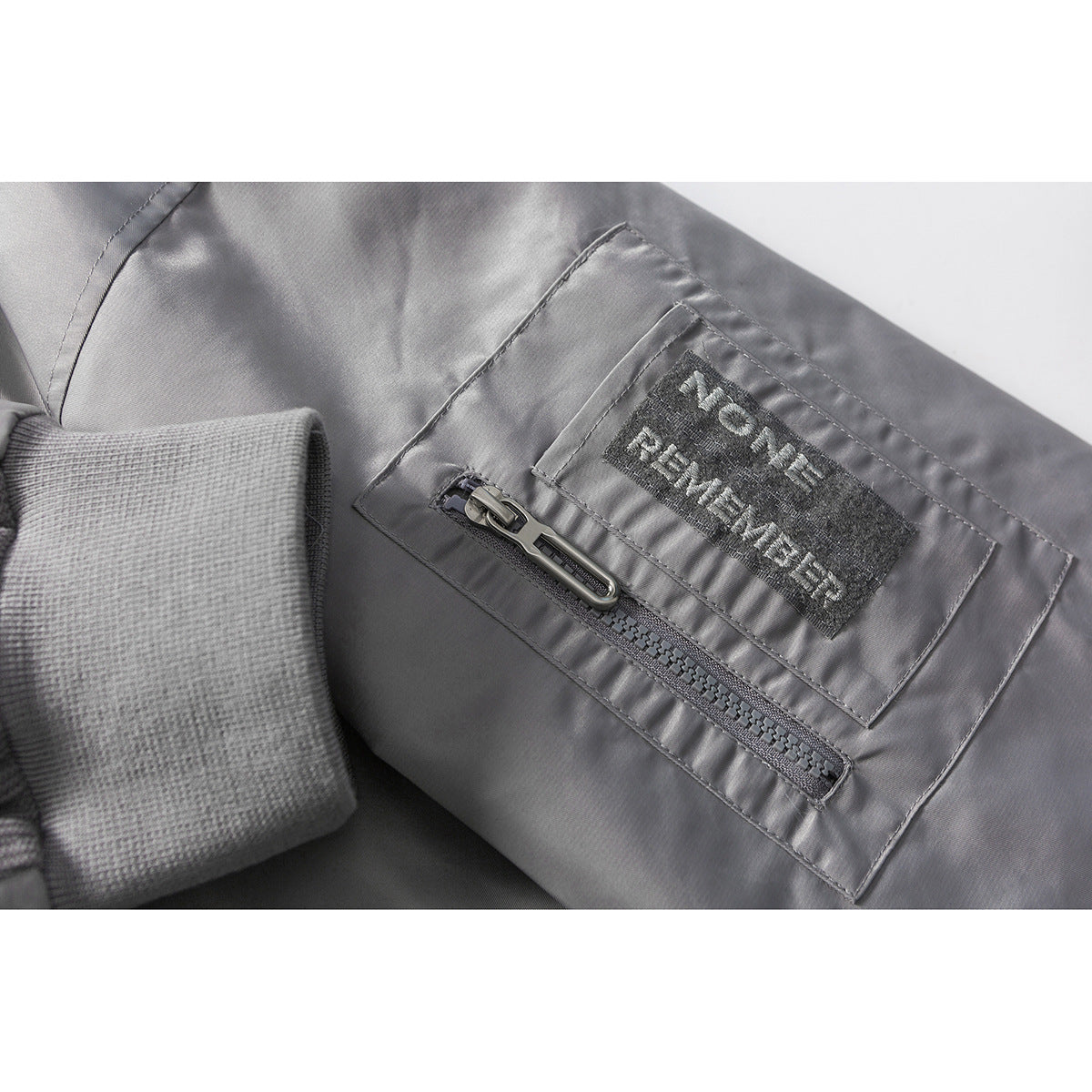 Close-up of a gray jacket sleeve pocket with a zipper and an English-text patch.