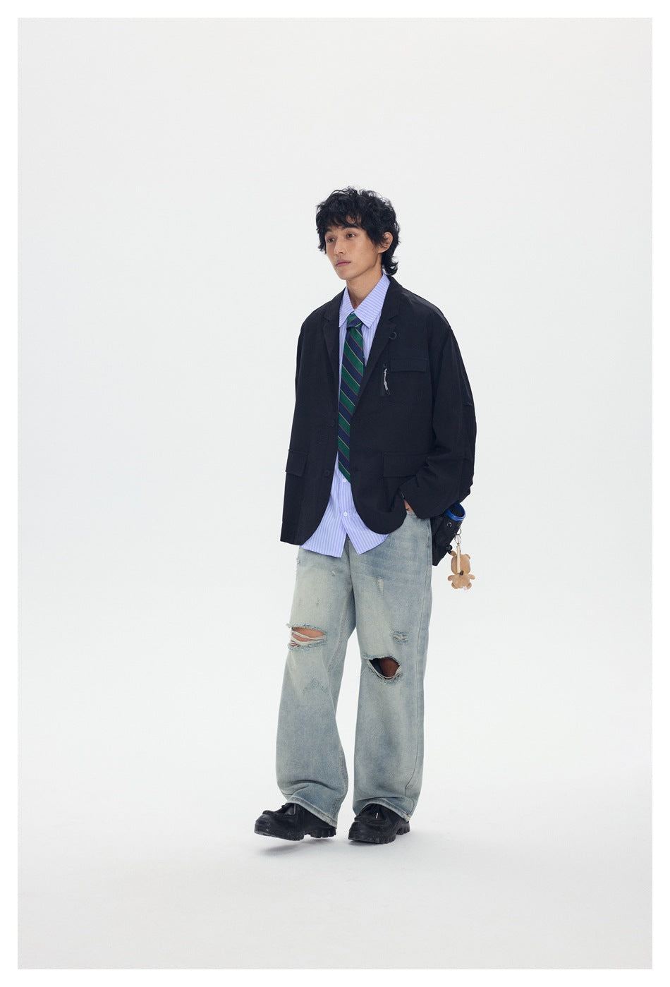 Full-length model wearing a black blazer, blue striped shirt, green striped tie, and distressed wide-leg jeans.
