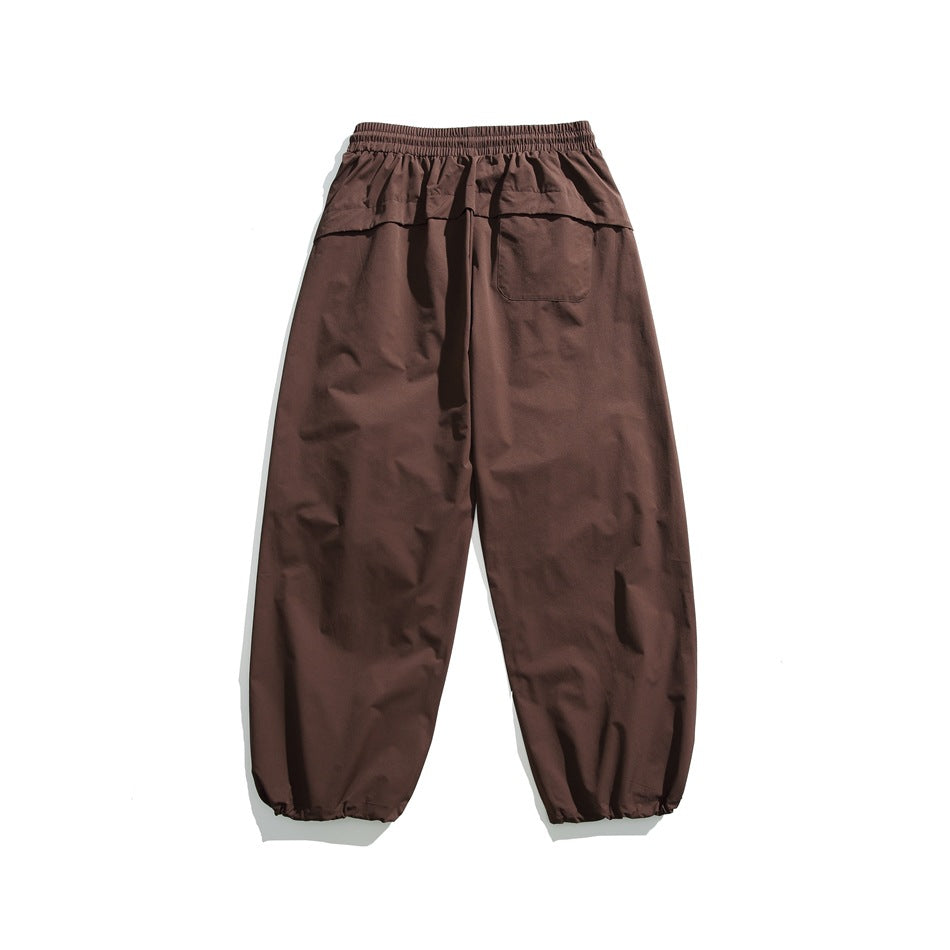 Rear view of dark brown loose trousers with an elastic waistband, one back pocket, and gathered ankle cuffs.