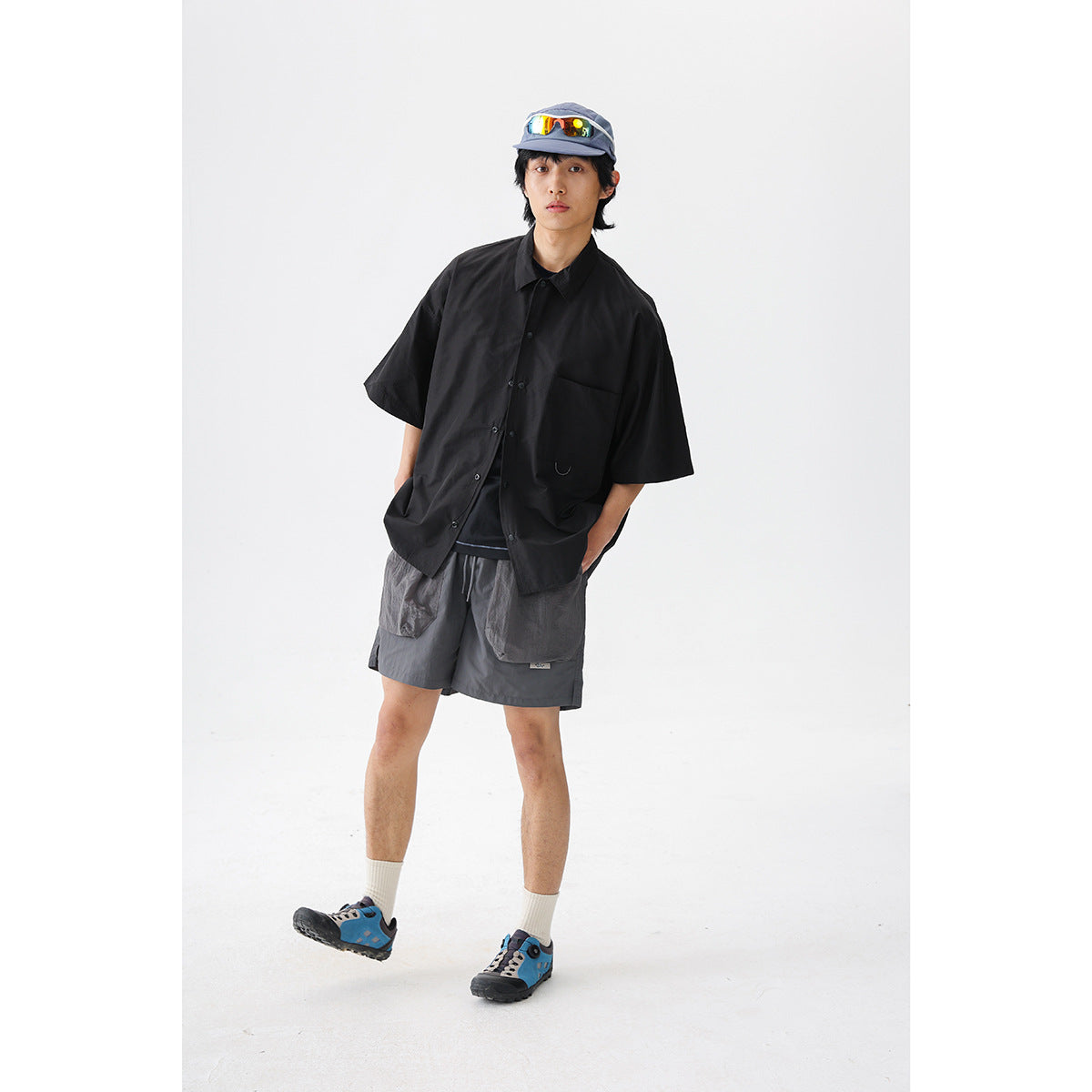 Model wearing a black short-sleeve button-up shirt and dark gray cargo shorts against a white studio background.