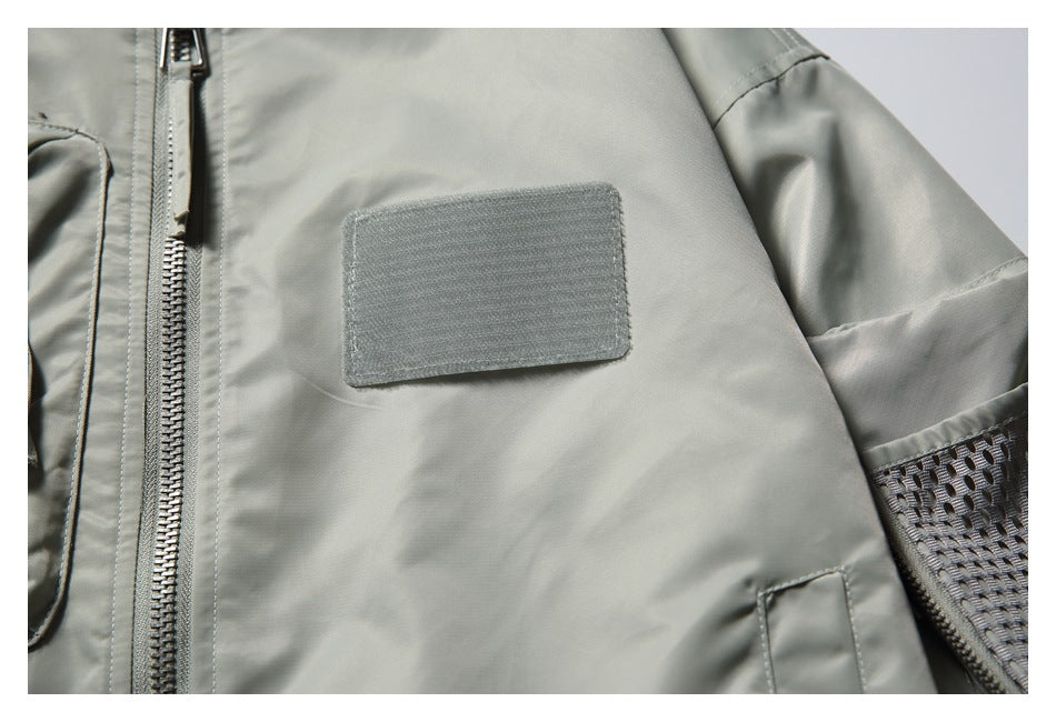 Close-up of a pale gray-green jacket front with a blank rectangular patch and mesh sleeve detail.