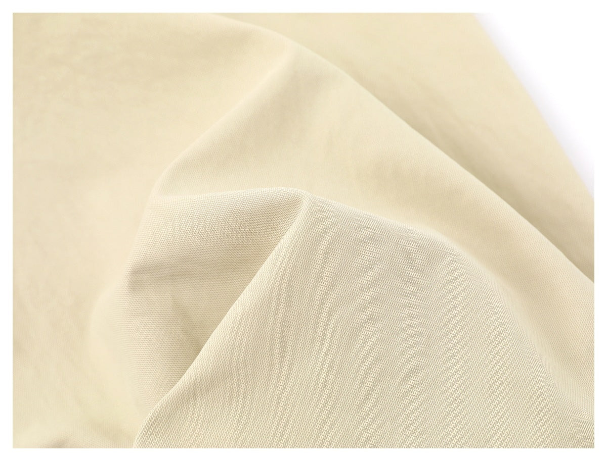 Extreme close-up of cream-colored trouser fabric, showing its fine woven texture and drape.