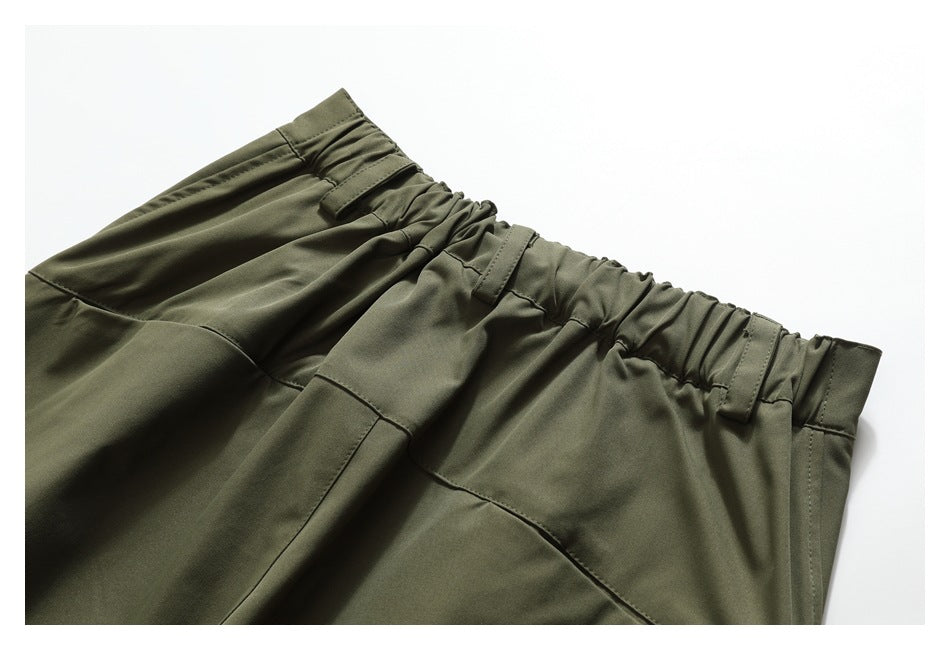 Close-up of olive-green pants showing the gathered elastic waistband, belt loops, and stitched panel seams.