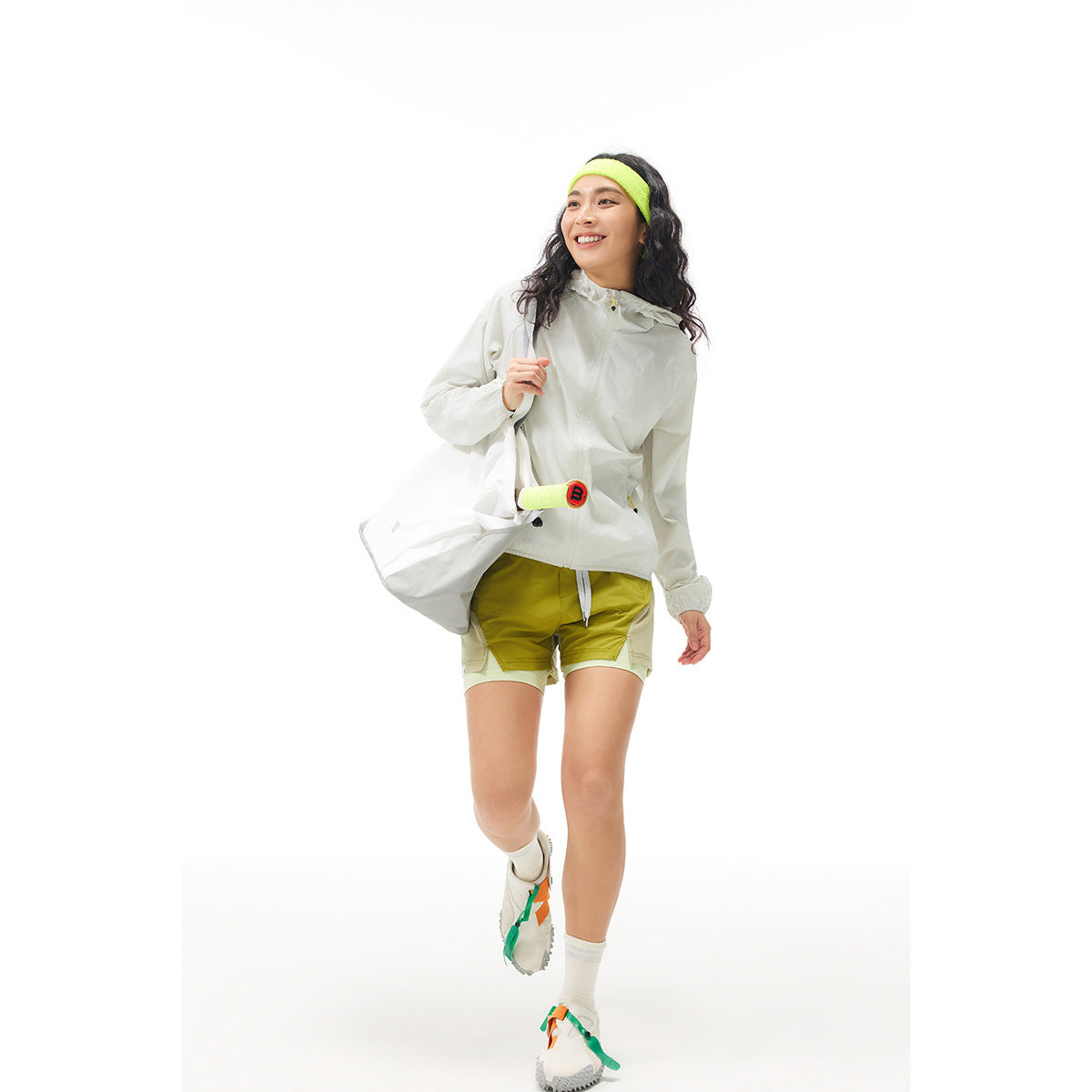 Woman wearing a white hooded jacket and yellow-green running shorts, with a matching neon headband.