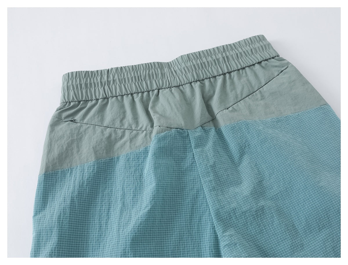 Back view of sage green pants with an elastic waistband and broad blue grid-patterned lower panels.