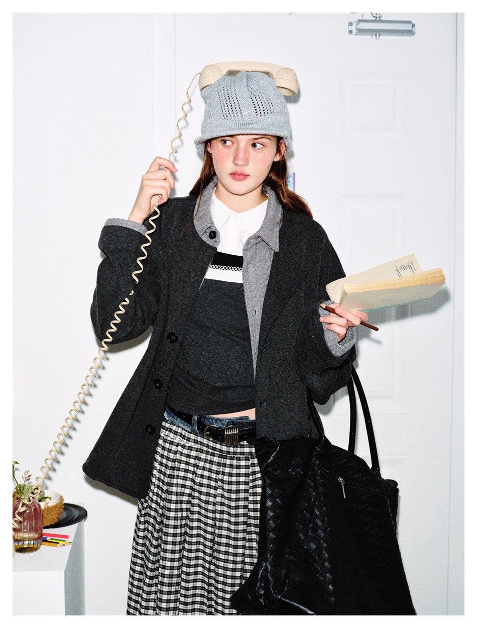 Model wearing a charcoal button-front jacket with gray collar and cuffs, a dark top, checked skirt and knit hat.