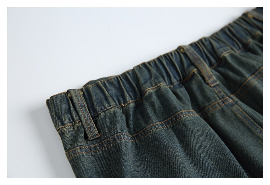Close-up of dark indigo denim trousers with a gathered elastic waistband, belt loop and brown stitching.