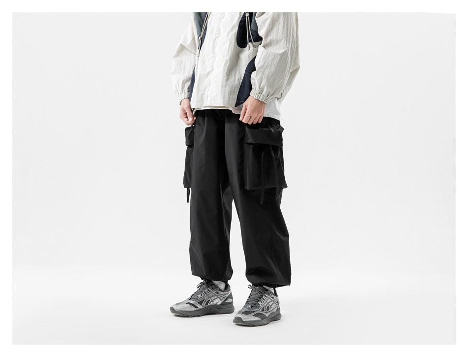 Cropped model wearing loose black cargo pants with large side pockets, elastic cuffs, and a white jacket.