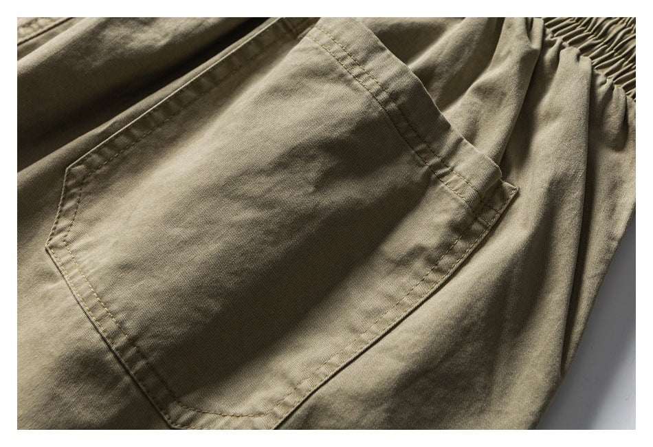 Close-up of a large stitched patch pocket on khaki shorts, with part of the elastic waistband visible.