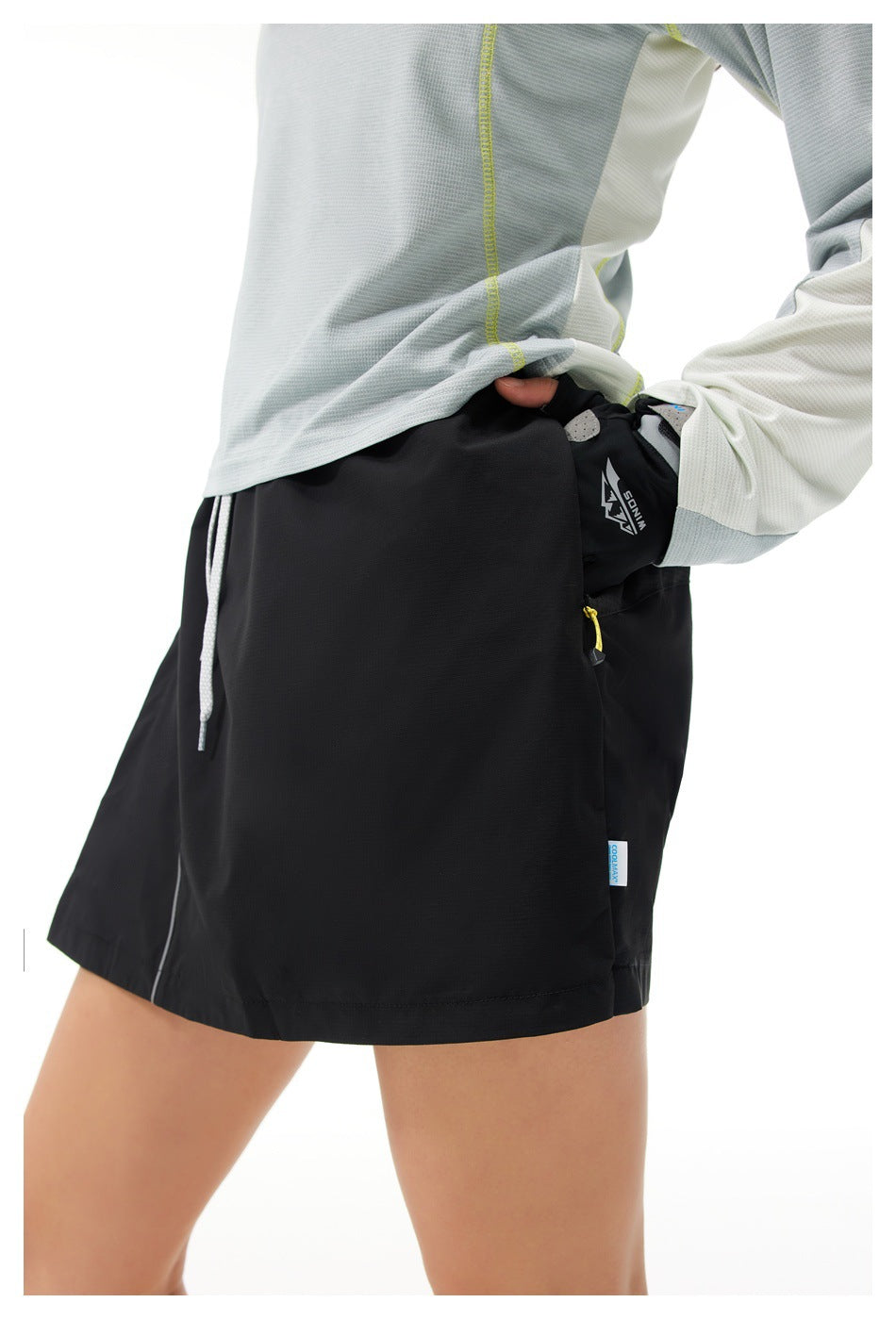 Close-up of a model wearing black athletic skort shorts with a yellow-zip side pocket.