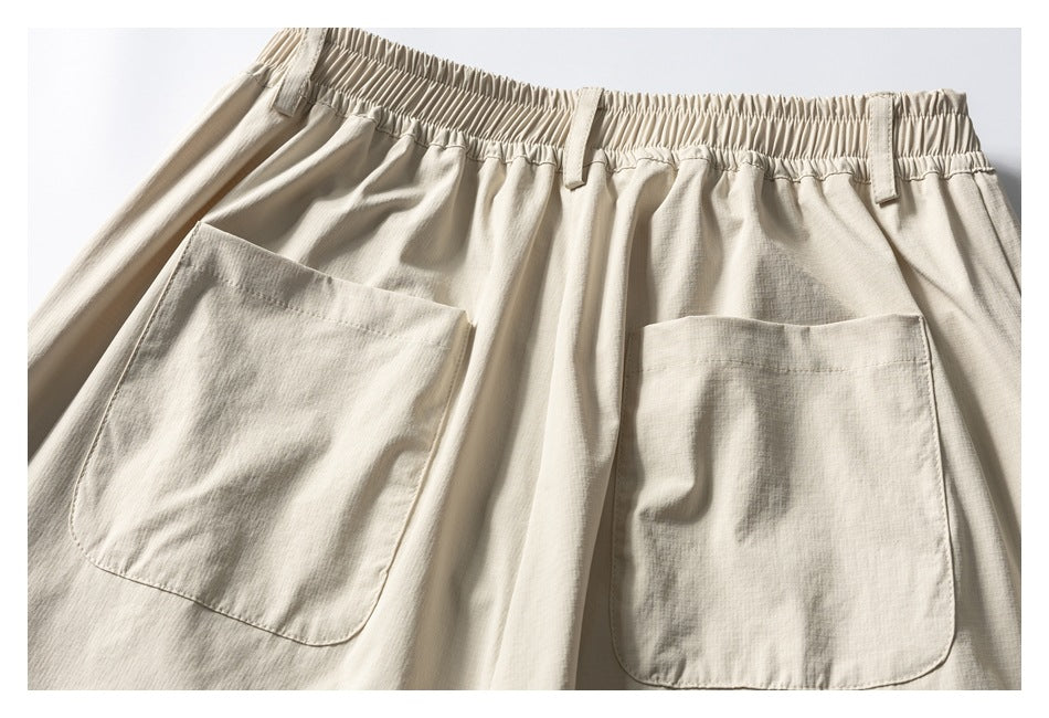 Flat lay back view of light beige trousers with a gathered elastic waistband and two large patch pockets.