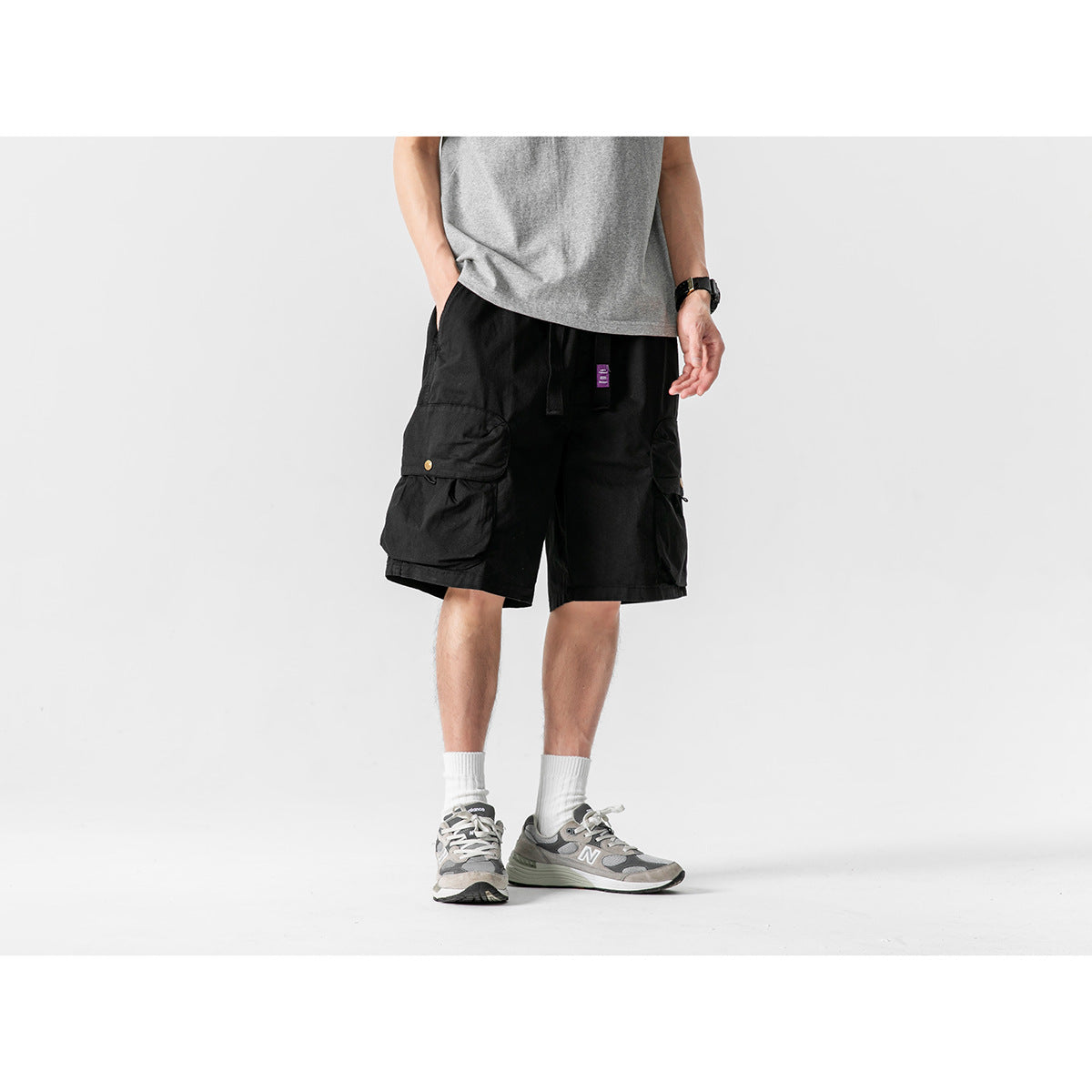 Front view of a model wearing black cargo shorts with large flap pockets and a drawstring waist.