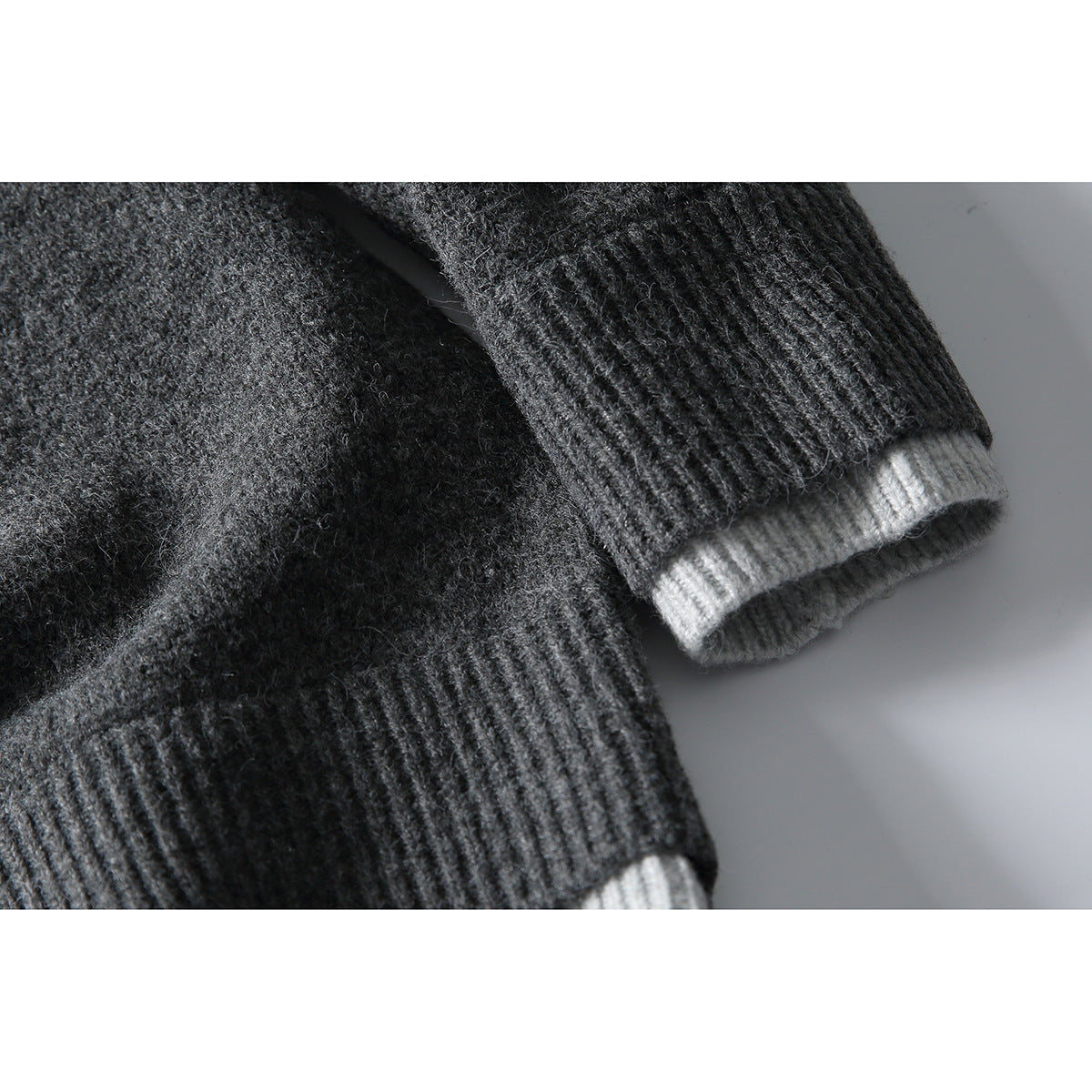Close-up of a charcoal sweater's ribbed cuff, with a light gray contrasting layer visible underneath.