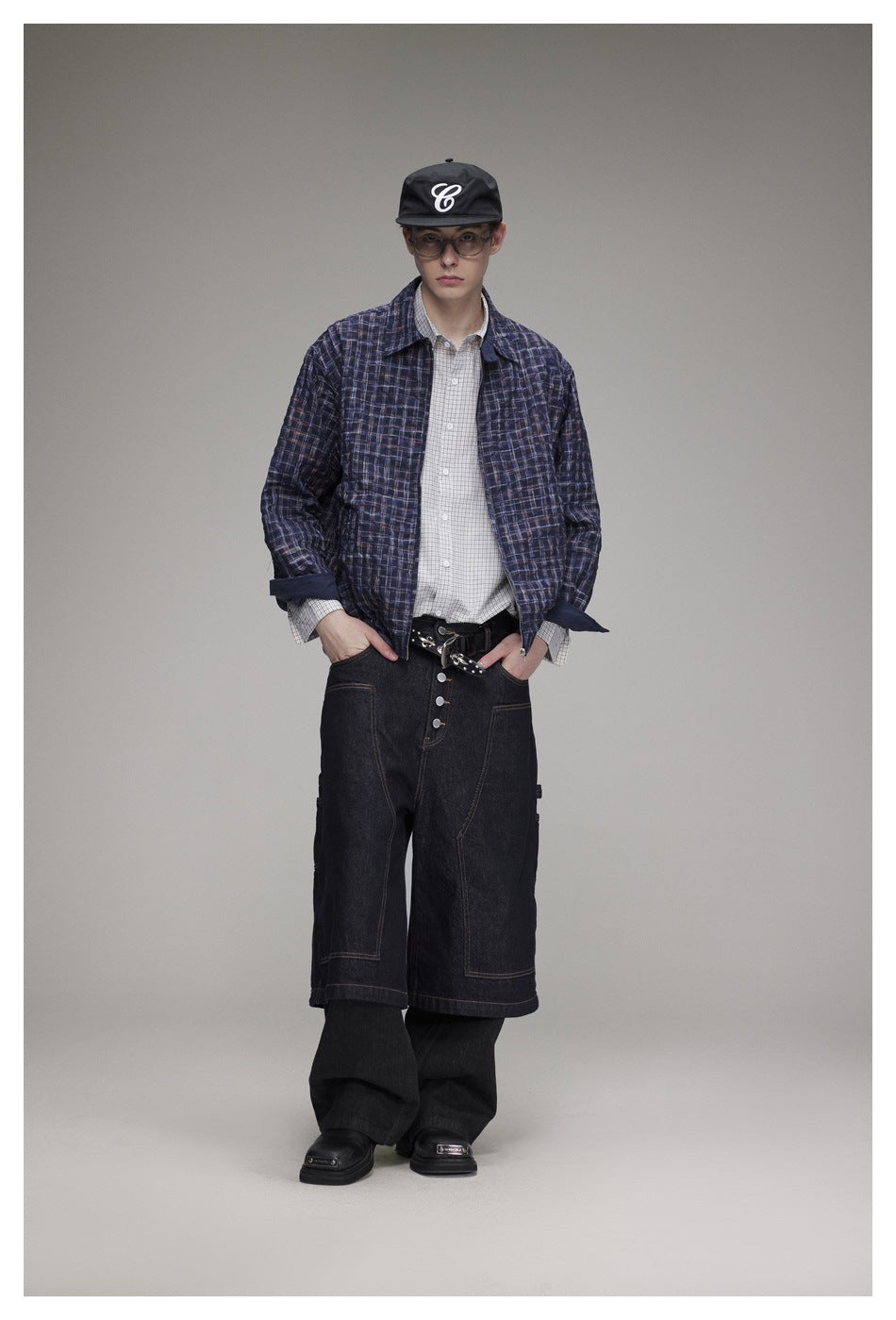 Front view of a model wearing a navy plaid jacket over a light checked shirt with dark wide-leg pants.