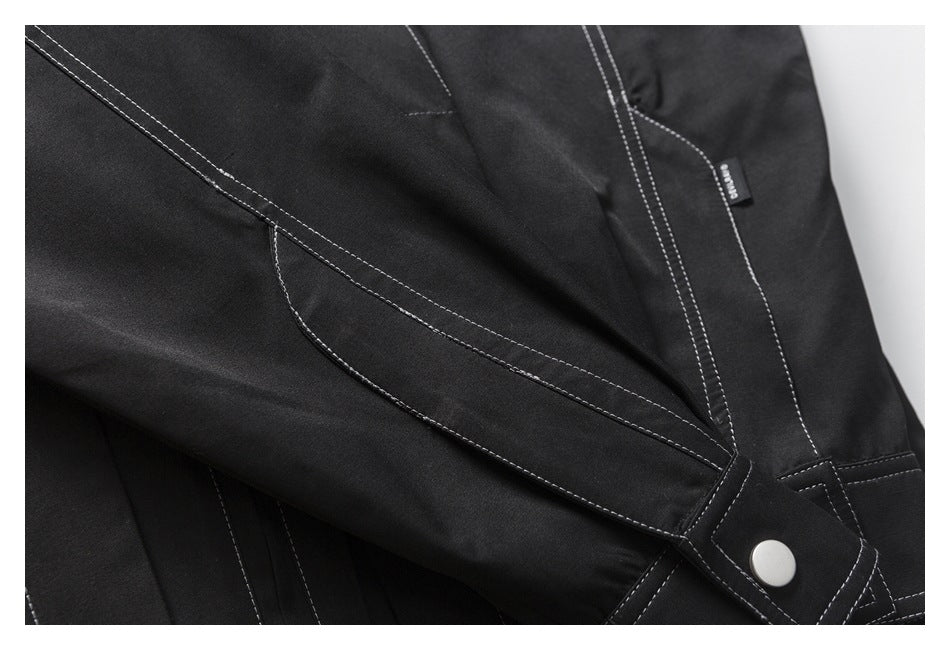 Close-up of a black sleeve with a snap-fastened tab, white contrast stitching, and a small fabric label.