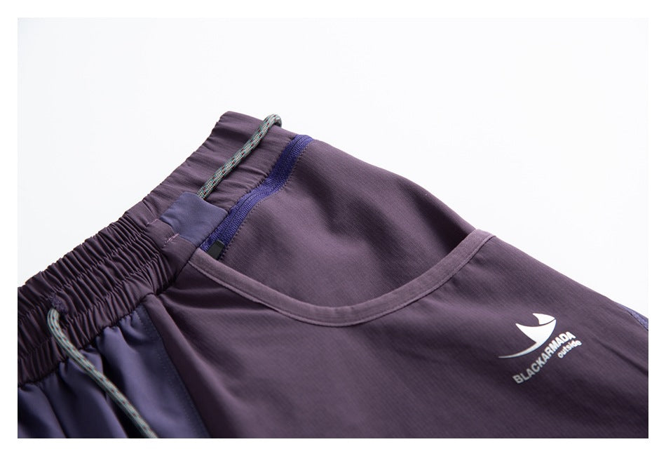 Close-up of a curved front pocket, contrast trim, drawcord, and small white logo on purple pants.