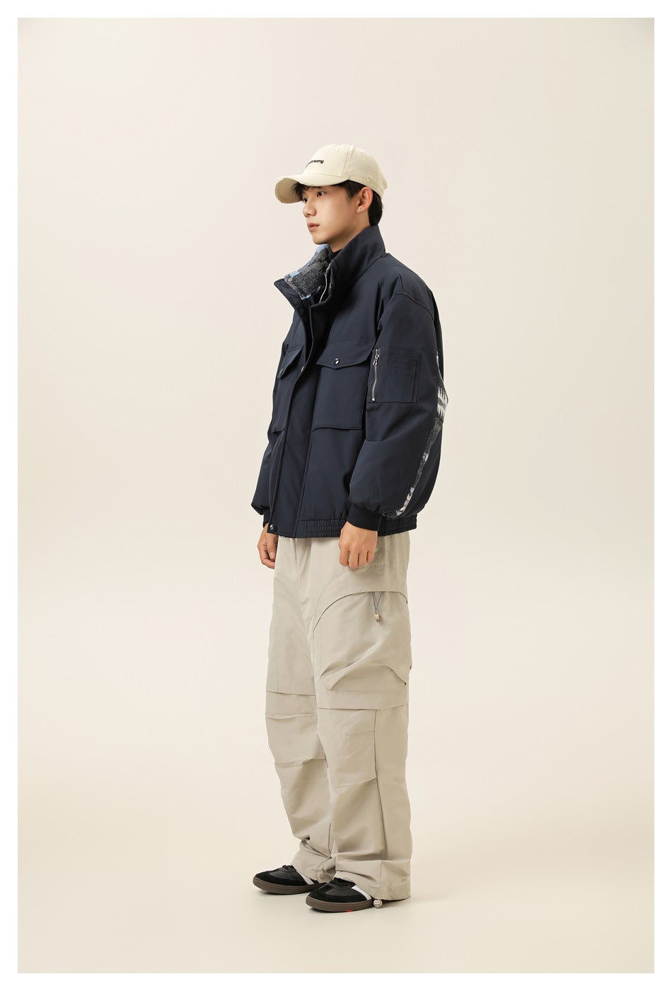 Side view of a model wearing a navy utility jacket with a high collar, roomy sleeves and cargo-style pockets.