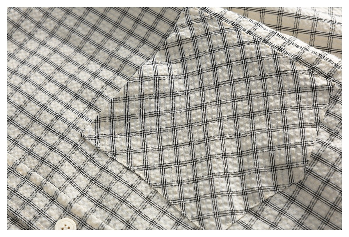 Close-up of a rounded patch pocket on an ivory shirt with a fine black plaid pattern.