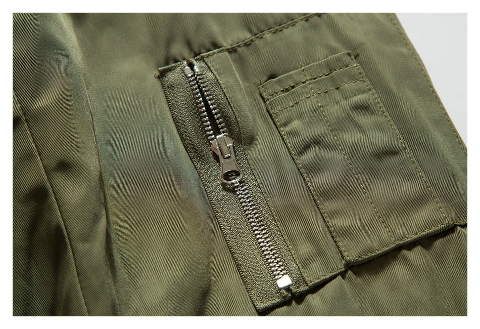 Close-up of an olive jacket sleeve pocket with a metal zipper and a narrow stitched pocket beside it.
