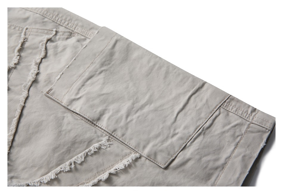 Close-up of light taupe trousers showing a large patch pocket and frayed fabric panel seams.