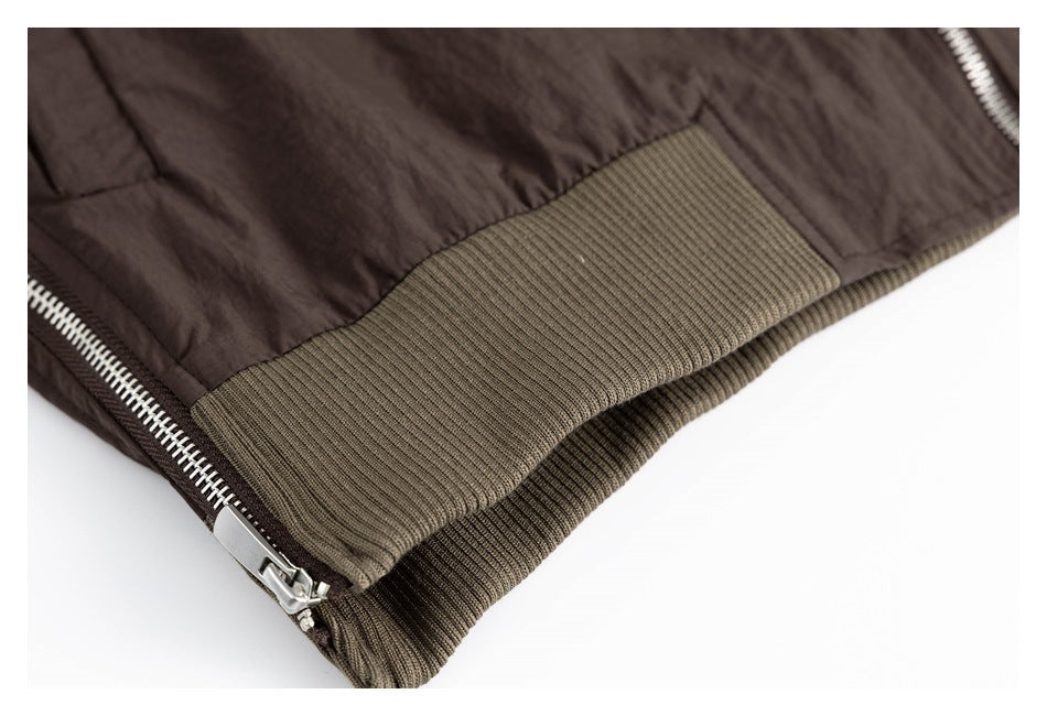 Close-up of a dark brown jacket hem with olive-brown ribbed trim and a silver zipper.