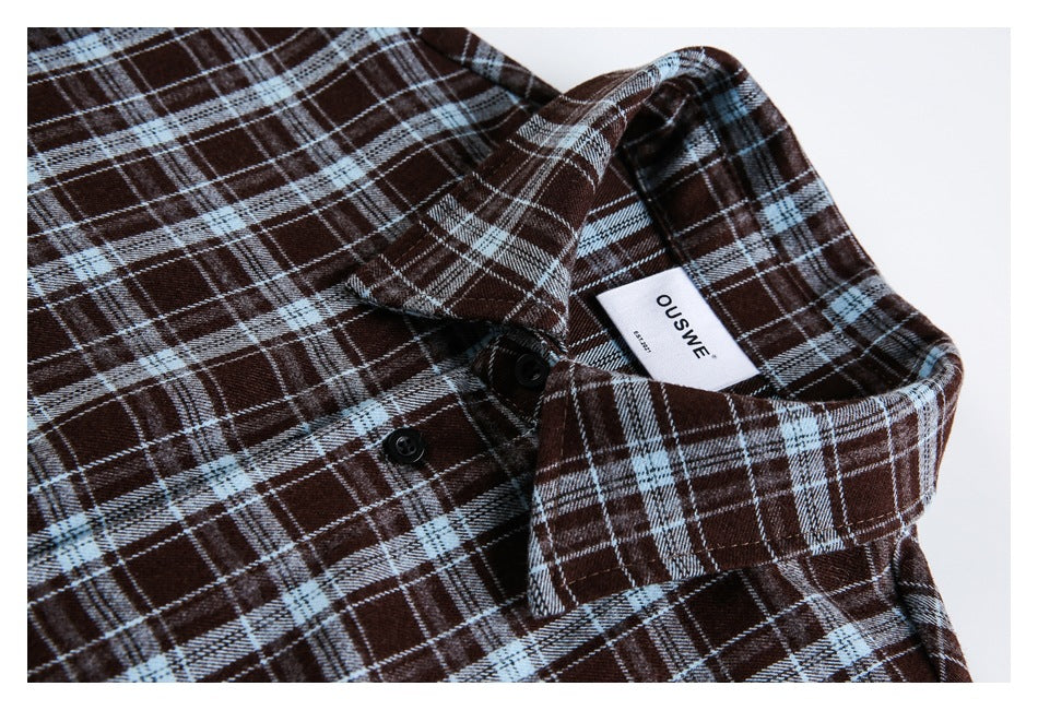 Close-up of a brown and pale blue plaid shirt collar, buttons, and sewn-in white label.
