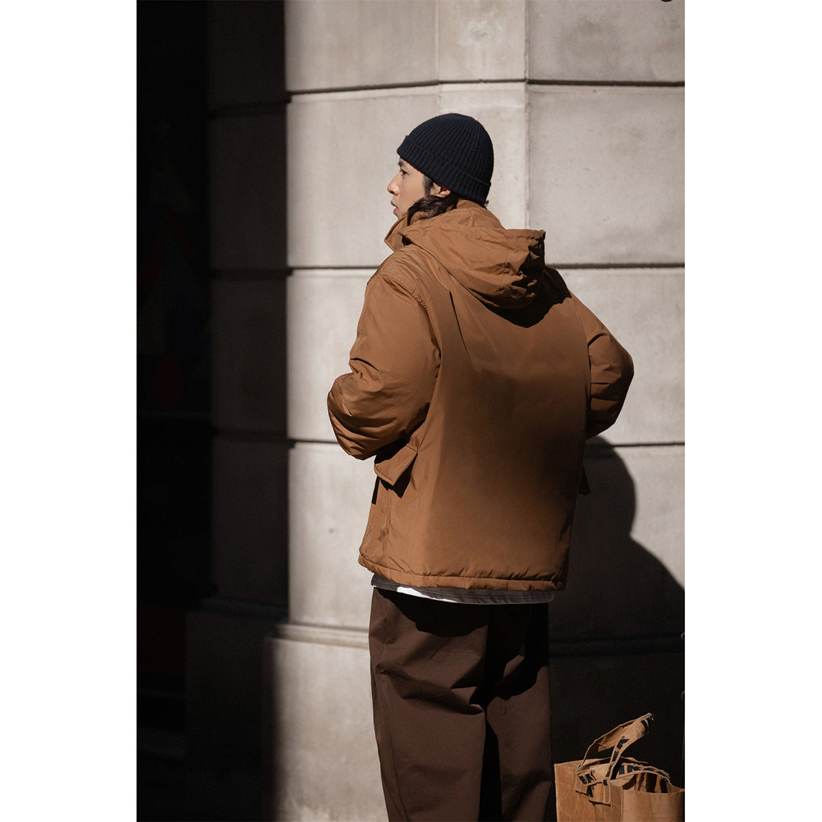 Rear view of a model wearing the brown hooded jacket, showing its plain back and relaxed fit.