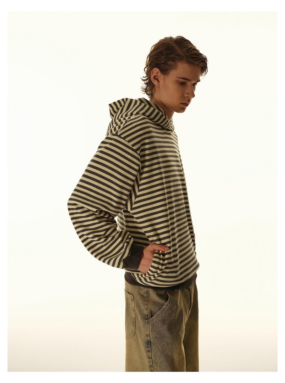Side view of a model wearing a loose beige and dark striped hooded sweatshirt with a dark ribbed hem.
