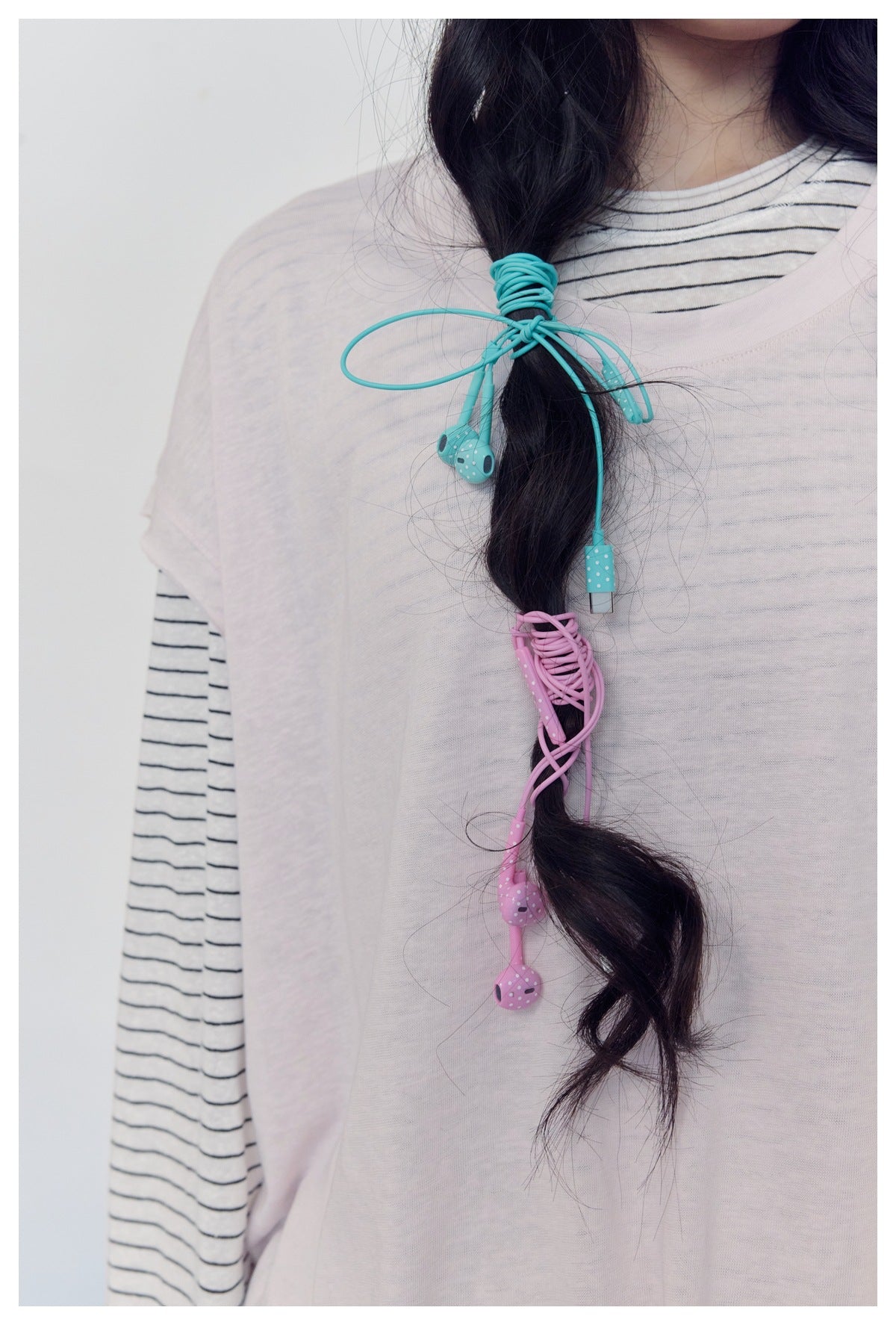 Close-up of a model in a pale top over a striped shirt, with turquoise and pink wired earbuds looped around her braid.