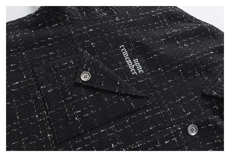 Close-up of a buttoned chest pocket and small white embroidered lettering on a black shirt with a flecked grid pattern.