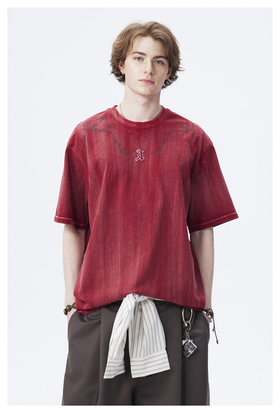 Model wearing an oversized faded red short-sleeve T-shirt with dark shoulder graphics and a small embroidered chest letter.