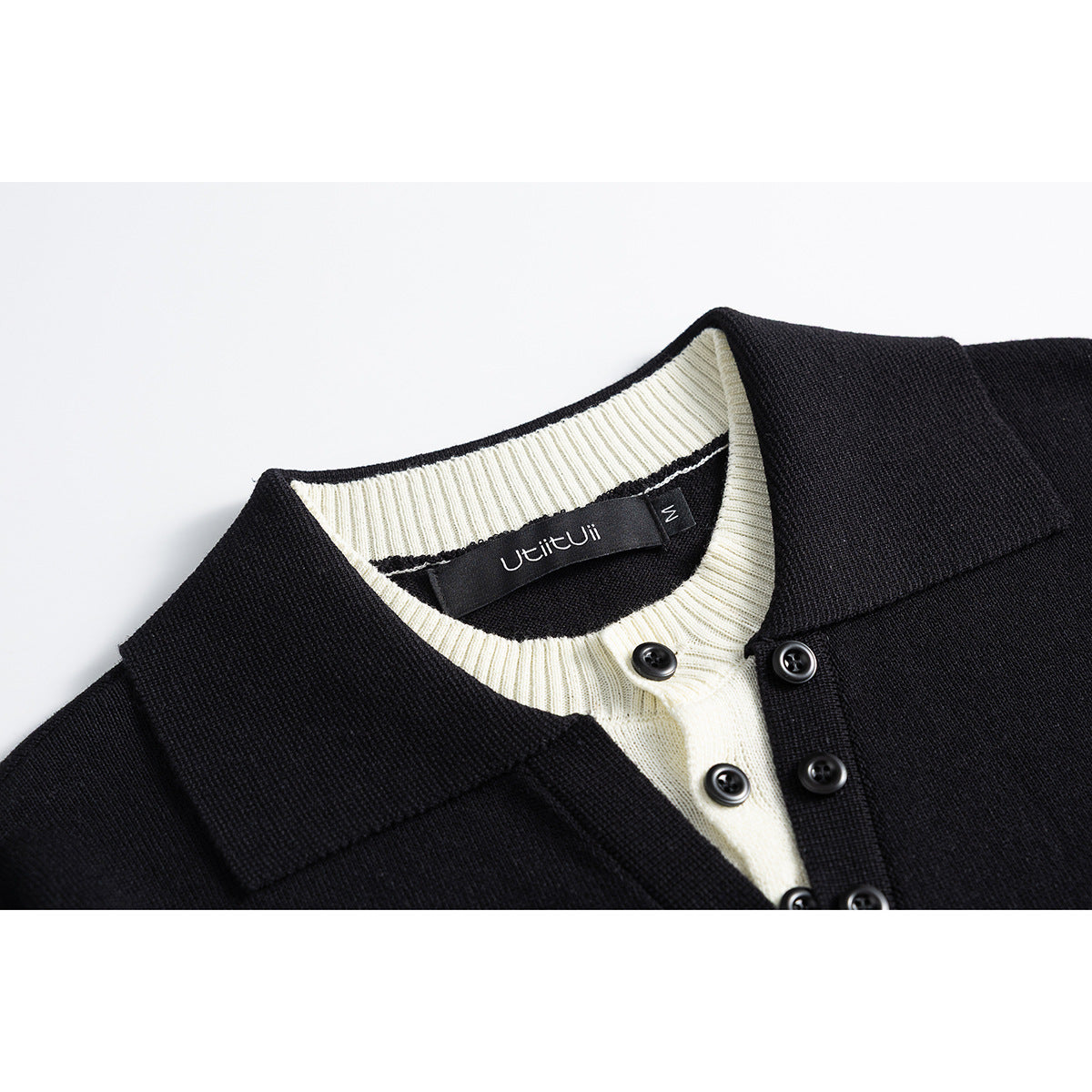Close-up of a black knit cardigan with a cream ribbed neckline, pointed collar, and black buttons.