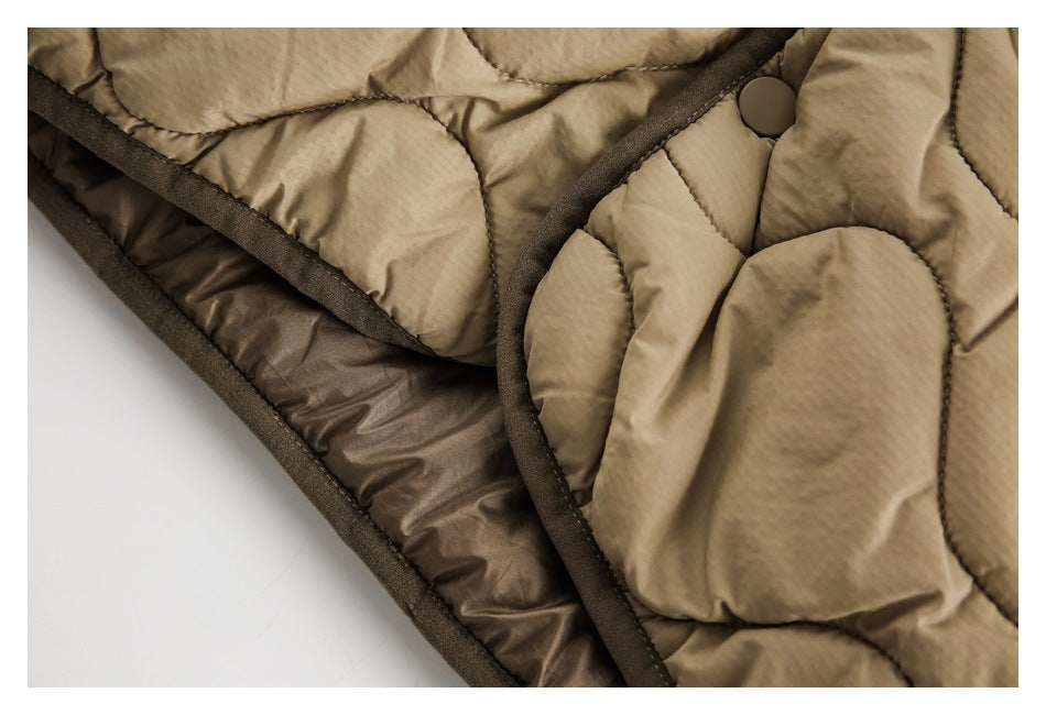 Close-up of tan quilted outerwear showing a dark snap, bound edges, and brown lining.