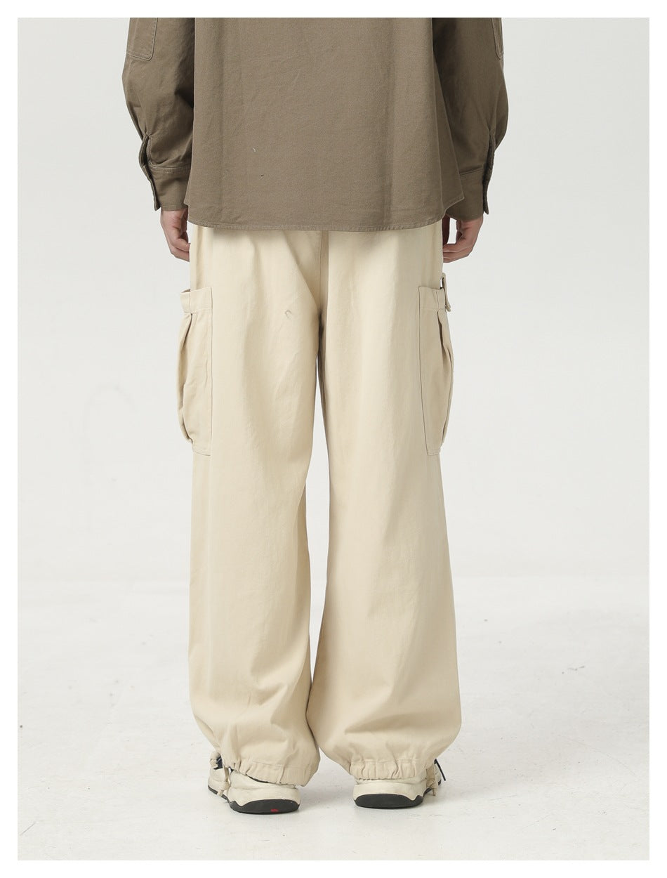 Back view of a model wearing loose cream cargo pants with side cargo pockets and elastic ankle cuffs.