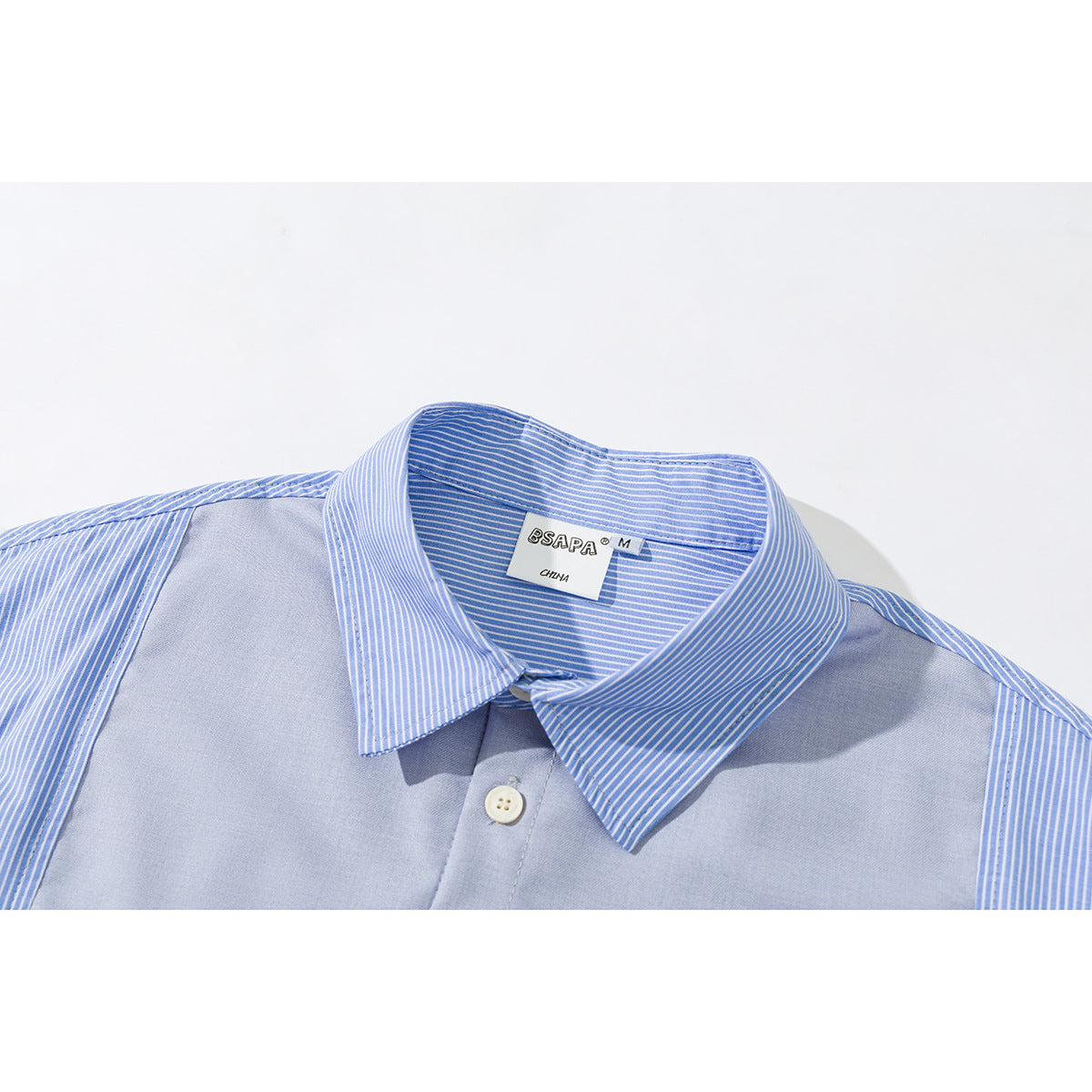 Close-up of a light blue shirt collar with blue-and-white striped panels and a button; neck label visible.