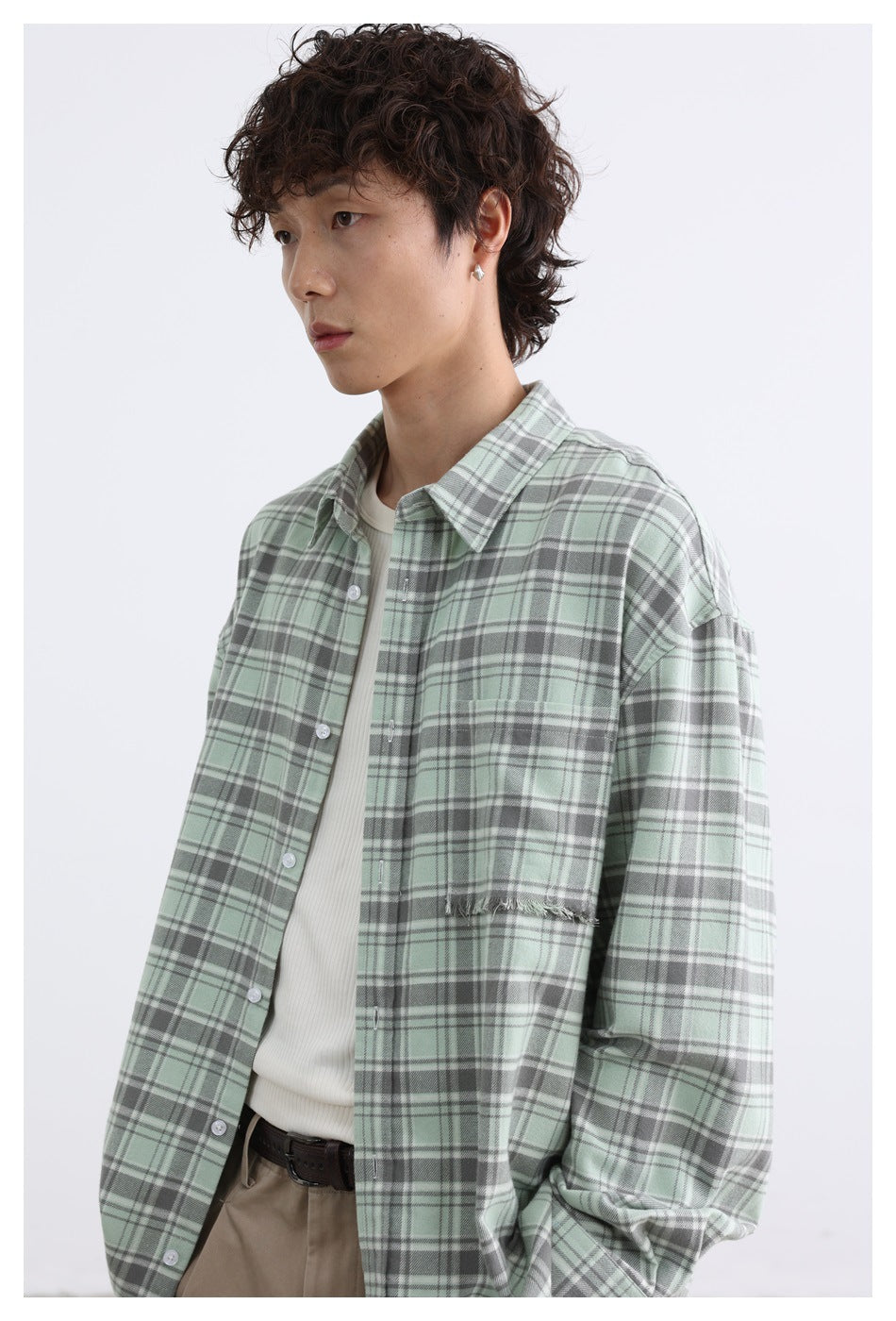 Close view of a model wearing a sage green plaid shirt, showing its collar, buttons, chest pocket, and frayed pocket edge.
